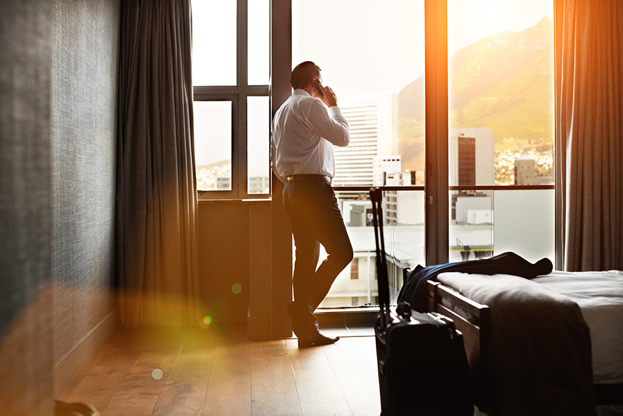 Rearview shot of a businessman looking through a hotel room window and talking on a cellphone.